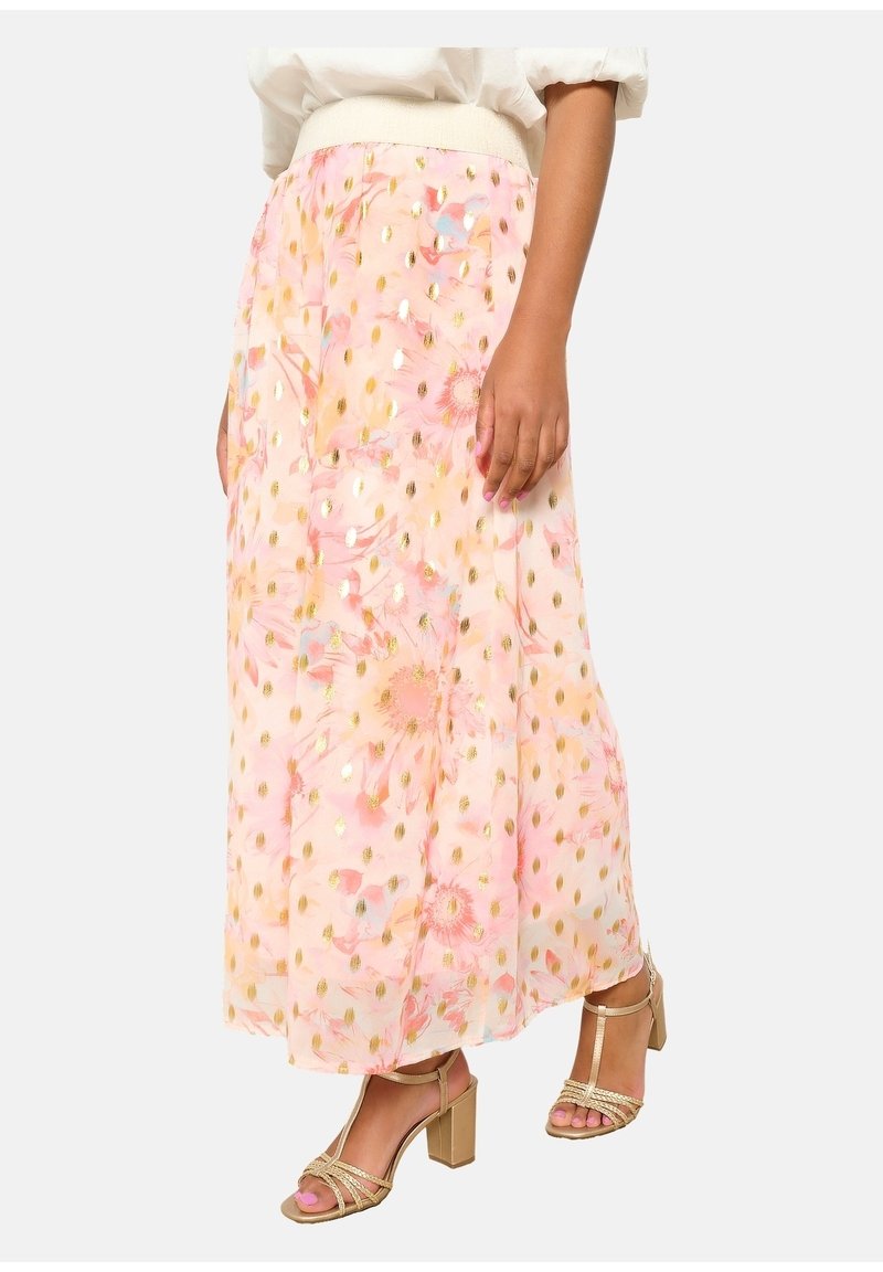 Jupe maxi florale rose en tissu texturé, ornée de motifs à pois dorés et dotée d'une ceinture élastique, accompagnée de sandales à talons blocs dorés.