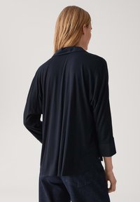 Camicia a maniche lunghe blu navy, con vestibilità ampia, spacco posteriore e colletto. Il tessuto appare morbido e liscio, con un design semplice.