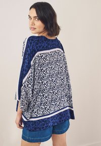 Marineblauwe en witte bloempatronen blouse met een oversized pasvorm, korte mouwen en contrasterende randen. Gepaard met denim shorts.