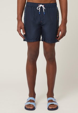 Marinefarbene Badeshorts mit verstellbarem Bund, die an den Seiten mehrfarbige vertikale Streifen aufweisen und aus leichtem, wasserabweisendem Material gefertigt sind.