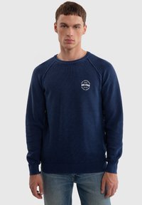 Námořnický modrý pletený svetr s texturovaným vzorem, žebrovanými manžetami a lemem, s bílým logem na levé hrudi. Pohodlný střih, kulatý výstřih.