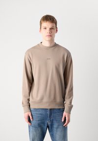 Sudadera marrón con cuello y puños acanalados, con un logo sutil en el pecho. Combinada con jeans azules, sobre un fondo liso.