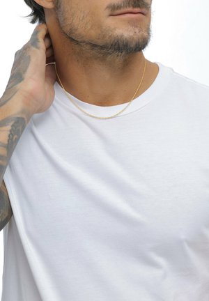 Guldtonet kæd necklace båret på en bar hals, med en simpel hvid bomulds t-shirt i baggrunden. Kæden har et delikat, struktureret udseende.
