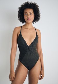 Μαύρο ολόσωμο μαγιό με βαθύ V ντεκολτέ, στριφτό μπροστινό σχέδιο και λεπτές τιράντες. Η ιριδίζουσα υφή προσθέτει οπτικό ενδιαφέρον.