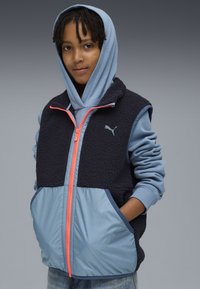 Marinefarbener Fleece-Westen mit hellblauem Saum, pinkem Reißverschluss, zwei frontalen Taschen und einem grauen Kapuzenpulli darunter. Mit Puma-Logo auf der Brust.