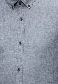 Ανοιχτό γκρι πουκάμισο με κουμπιά και γιακά με κουμπιά, με ορατή ραφή σε υφασμάτινη υφή.