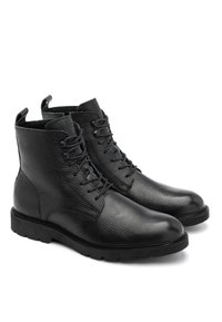 Czarne skórzane botki do kostki charakteryzują się fakturą wulkanizowaną, sznurowanym zapięciem oraz solidną gumową podeszwą z pętelkami z tyłu, ułatwiającymi zakładanie.