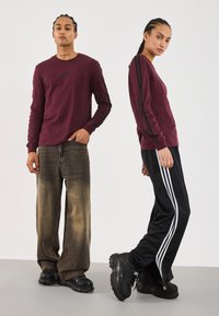 Langermede burgunder skjorter med svarte sidestriper, kombinert med løse falmede brune jeans og svarte sneakers. Minimalistisk design og avslappet stil.