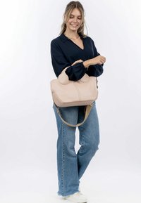 Borsa a mano in pelle beige con accenti laterali arrotondati, doppi manici, tracolla regolabile e semplice dettagli di cucitura.