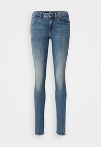 Jeans de denim azul ajustados con un acabado desgastado, cuatro bolsillos y cierre de botón metálico. Presenta un ligero desgarro y una textura suave.