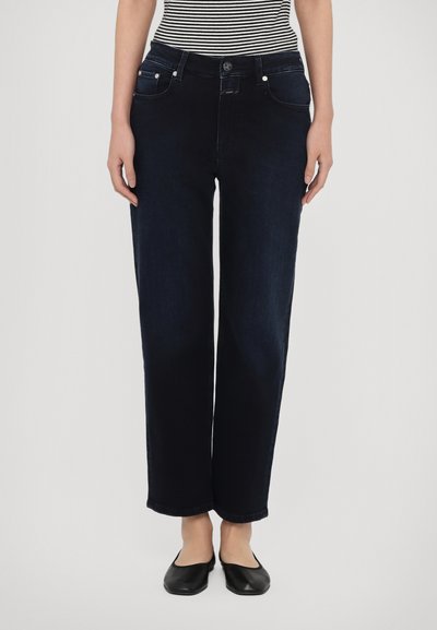 Dunkelblaue Jeans mit lockerem Schnitt, ausgestattet mit Vordertaschen, einem Knopfverschluss und umgeschlagenen Säumen. Flache schwarze Schuhe runden den Look ab.