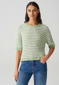 Pull rayé vert et blanc, texturé, avec des manches courtes et un col rond, associé à un jean en denim bleu.