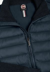 Námornícka modrá prešívaná bunda so zipsom, pleteným golierom a manžetami a s označením Colmar Originals vo vnútri goliera.