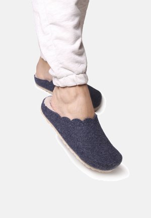 Navy felt slippers with a scalloped edge, soft lining, and a light rubber sole; paired with light-colored cuffed pants.