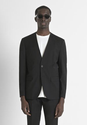 Schwarzer maßgeschneiderter Blazer mit einem einzelnen Knopf, geschlitzten Reverenzen und zwei vorderen Taschen, kombiniert mit einem weißen Rundhalsausschnitt-T-Shirt.