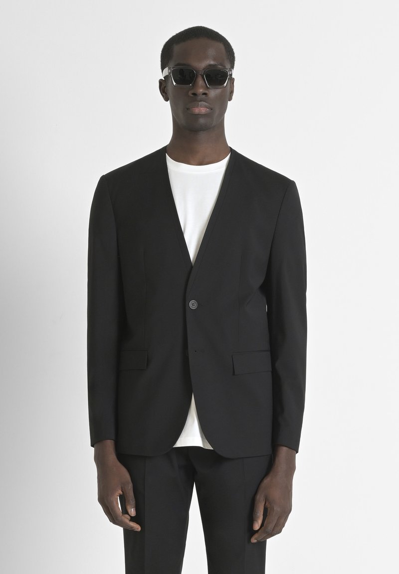 Blazer nero su misura con un bottone singolo, rever a punte e due tasche frontali, abbinato a una maglietta bianca a girocollo.