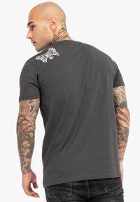 Graues Baumwoll-T-Shirt mit kurzen Ärmeln und Rundhalsausschnitt. Verfügt über ein weißes grafisches Design im oberen Rückbereich. Glatte Textur, normale Passform.