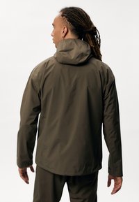 Oliven grøn vandtæt jakke med hætte, med en glat overflade og enkelt design, vist fra ryggen med elastiske ærmer.