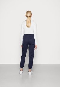 Marinblå joggingbyxor i mjukt material, med resårmidja, avsmalnande ben och muddar vid anklarna, i kombination med vita sneakers.