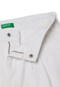 Bílé bavlněné kalhoty mají zipový zip, zapínání na knoflík a viditelné švy. Na etiketě je uvedeno "United Colors of Benetton."