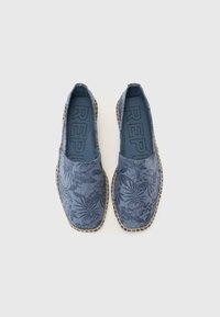 Espadrile din pânză albastră cu un model floral, margine țesută bej și talpă plată. Interiorul are o branț texturat albastru.