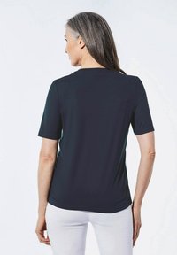 Zwarte korte mouwen t-shirt, zachte stof, ronde hals, gladde textuur, getailleerde pasvorm, gedragen met witte broeken, eenvoudig ontwerp.