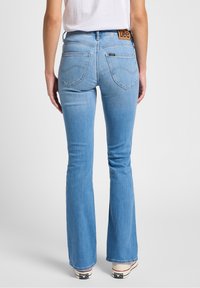 Jean évasés bleu clair avec une taille basse, dotés de poches arrière cousues et d'un label de marque beige au niveau de la taille.