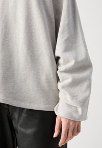 Maglione grigio chiaro a maniche lunghe con una consistenza morbida, caratterizzato da una vestibilità rilassata e polsini arrotolati, abbinato a pantaloni in pelle nera.