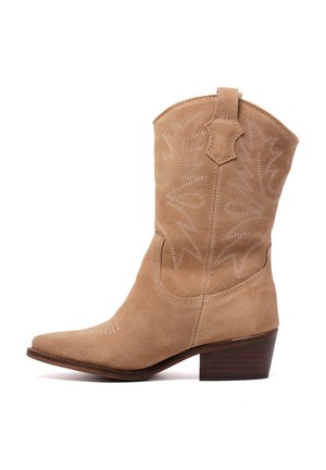 Botas de vaquero de ante en tono marrón claro con punta afilada, costuras decorativas y un tacón de madera apilada. Cuentan con una pestaña en la parte superior para ponérselas fácilmente.