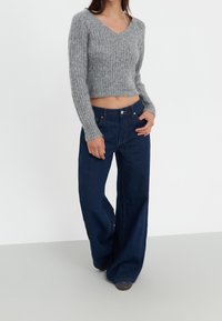 Pull gris côtelé court à col en V associé à un jean bleu foncé taille haute à jambes larges. Les deux pièces ont une coupe décontractée.