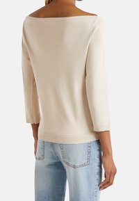 Beige, avskuren tröja med trekvartslånga ärmar. Ribbad textur längs halsringning och fåll, tillsammans med ljusblå jeans.