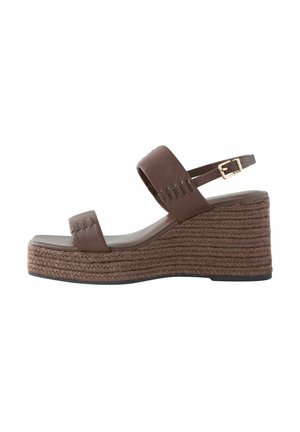 Brown wedge sandal with a woven rope sole and a single strap across the foot, featuring an adjustable buckle on the ankle.