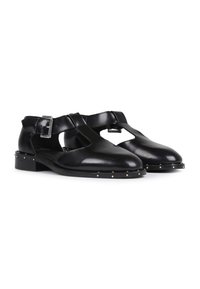 Schwarze Lederschuhe mit ausgeschnittenen Seiten, ausgestattet mit einem Riemen mit Schnalle, niedrigem Absatz und mit Nieten verzierte Sohle. Glatte Textur.