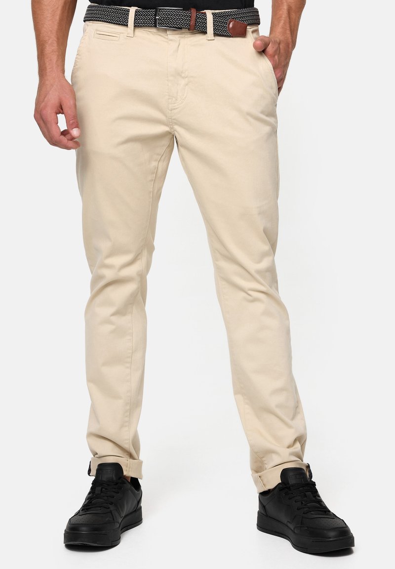 Chinos de algodón beige con corte recto, dobladillos levantados y bolsillos laterales. Combinados con zapatillas negras y un cinturón con estampado.