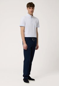 Hvid polo-shirt med mønstret krave og blå accenter, parret med mørkeblå bukser. Sættet har en afslappet pasform og teksturerede materialer.