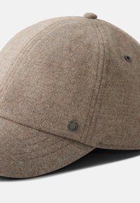 Bruine wollen pet met een gladde textuur, gestructureerde ronde kroon en een kleine bovenknop. Heeft gestikte naden en een metalen logo-accent.