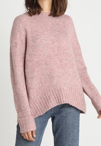 Rosa gestrickter Pullover mit lockerem Sitz, geripptem Saum und Bündchen. Weiche Textur, Rundhalsausschnitt und hinten etwas länger.