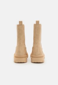 Bottes de cheville en daim beige avec une finition texturée, des côtés élastiques et des semelles en caoutchouc épaisses. Tirant renforcé à l'arrière pour un enfilage facile.
