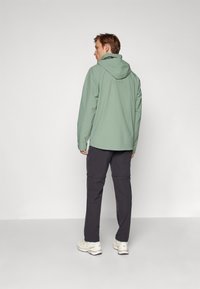 Hellgrüne Kapuzenjacke mit langen Ärmeln, kombiniert mit dunklen Hosen und weißen Sneakers. Glatte Textur; lässiges, funktionales Design.