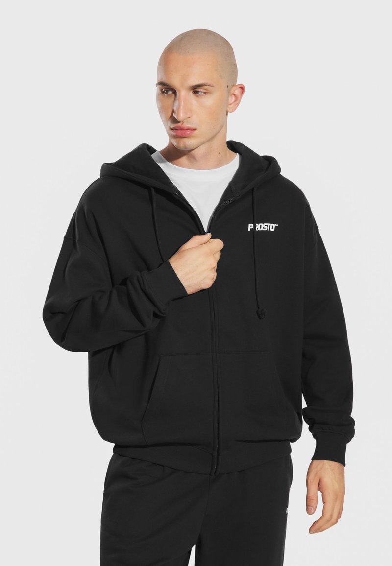 Czarna bluza z kapturem na zamek, wykonana z miękkiego materiału, z dużym kapturem, przednimi kieszeniami oraz białym logo "PROSTO" na lewej piersi.