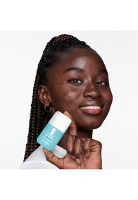 Clinique fuktighetsgel i en turkis beholder med et hvitt lokk, holdt av en person med flettet hår. Glatt tekstur, minimalistisk design.