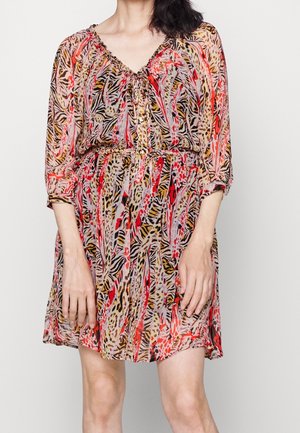Frau trägt ein knielanges, mehrfarbiges Kleid mit Animalprint, dreiviertel durchsichtigen Ärmeln und einem gerafften Ausschnitt mit Knöpfen.