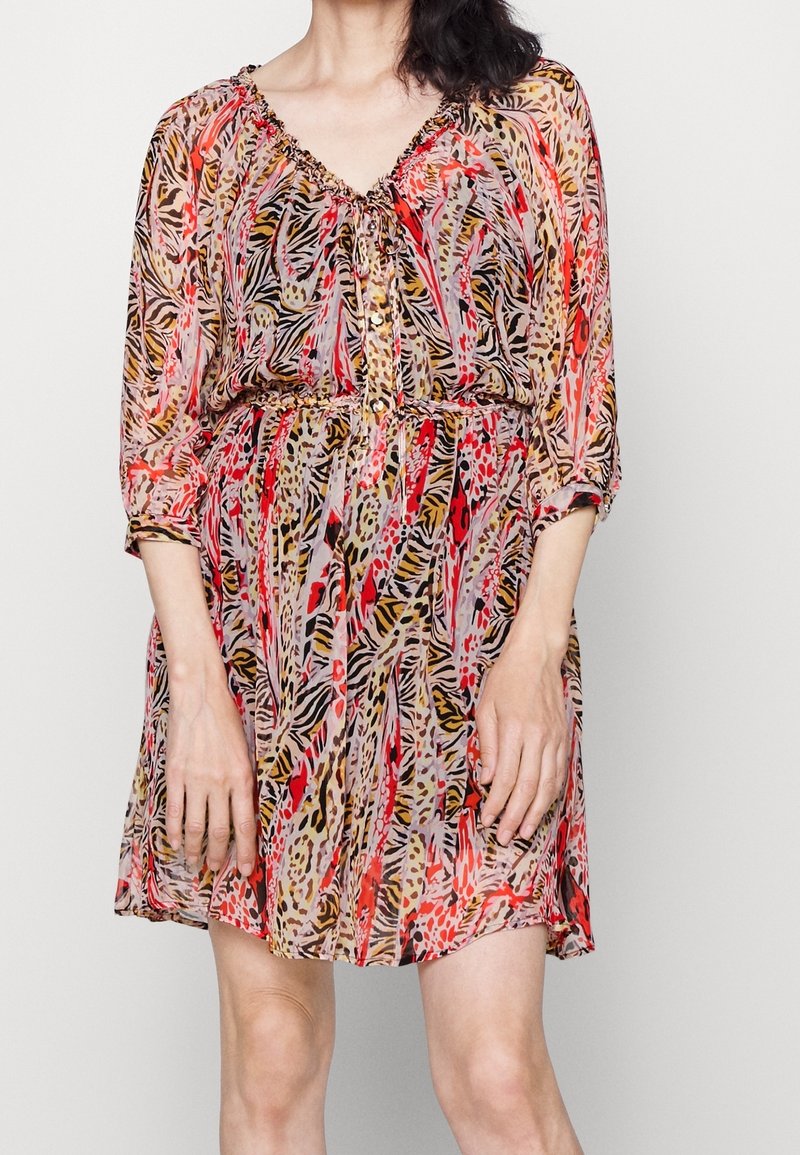 Femme portant une robe imprimée animal multicolore, longueur genou, avec manches transparentes trois-quarts et un col froncé avec des boutons.