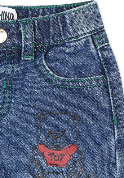 Shorts en denim avec des coutures vertes, présentant une poche frontale et un imprimé ours en peluche en noir et rouge sur le côté droit.