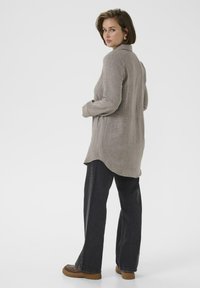 Maglietta a maniche lunghe grigia chiara con una vestibilità rilassata, orlo curvo e tessuto strutturato. Abbinata a jeans scuri a gamba larga e scarpe slip-on marroni.