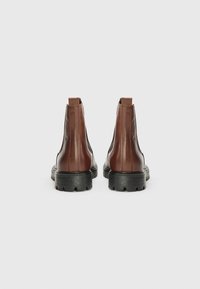 Bottines Chelsea en cuir marron avec semelles en caoutchouc noires, présentant une texture lisse, des panneaux latéraux élastiques et une languette pour un enfilage facile.