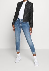 Svart läderbikerjacka med en figursydd design, kombinerad med slitage-ljusblå skinny jeans och vita sneakers. Vit t-shirt under.