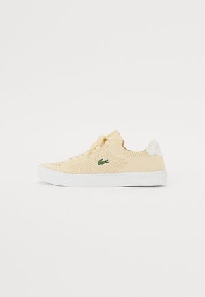Zapatillas de punto amarillas con una superficie texturizada, suela de goma blanca y un logo de cocodrilo verde en el lateral. Diseño casual, con cordones.