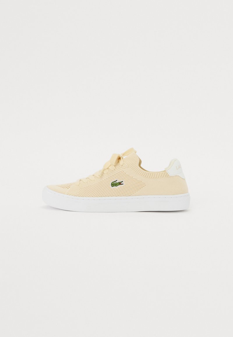 Kollane kudum sneaker, millel on tekstureeritud pind, valgest kummist tald ning roheline krokodilli logo küljel. Igapäevane, liputamisdisain.