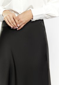 Schwarzer Satinrock mit einer glatten Textur und leichtem Glanz, mit einer Seitennaht und einer taillierten Taille, kombiniert mit einem weißen Hemd mit Knöpfen.